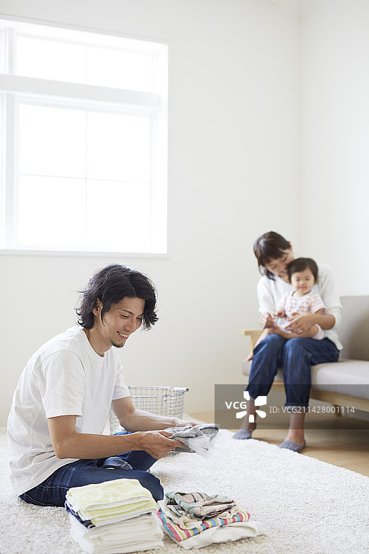 母亲和婴儿坐在沙发上，父亲在叠衣服图片素材