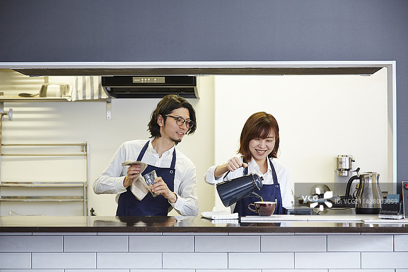 女服务员倒咖啡，男服务员在一旁观看图片素材