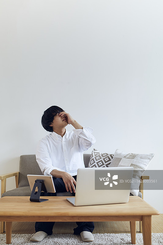 男人在客厅里电脑和平板前抱着头图片素材