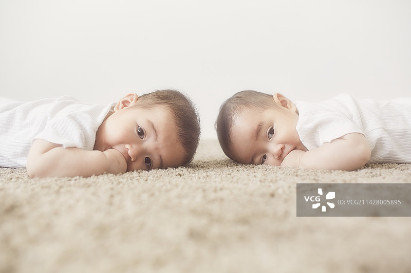 躺在米色地毯上吮吸手指的婴儿双胞胎图片素材