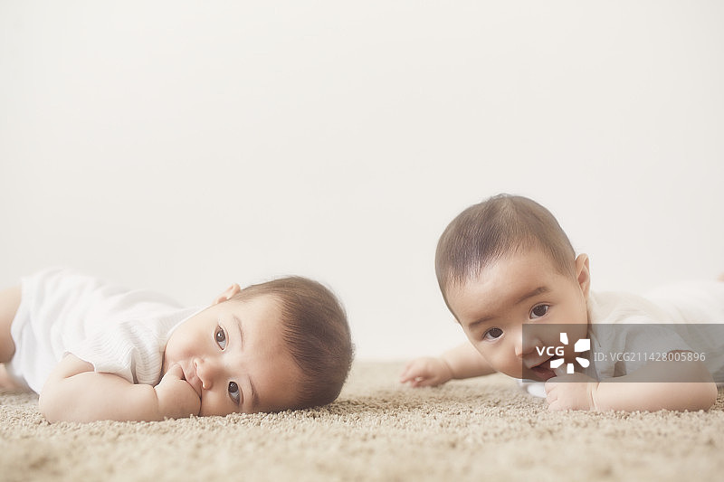 躺在米色地毯上吮吸手指的婴儿双胞胎图片素材