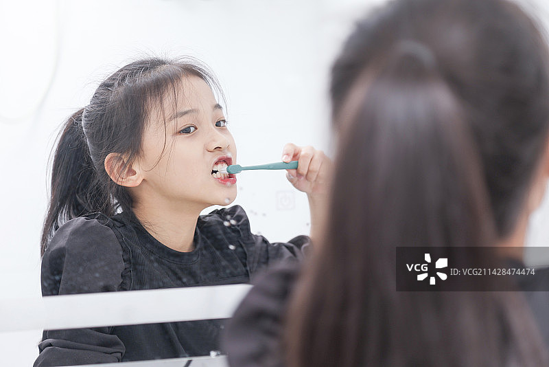 卫生间镜子里使用牙刷的小女孩图片素材