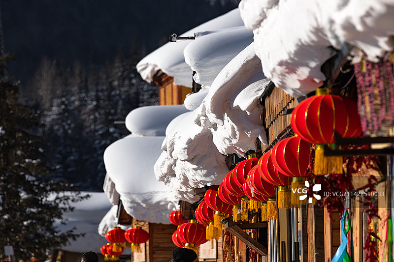 冬天里晴朗的天气，黑龙江雪乡，村子屋顶厚厚的积雪和屋檐下的大红灯笼。图片素材