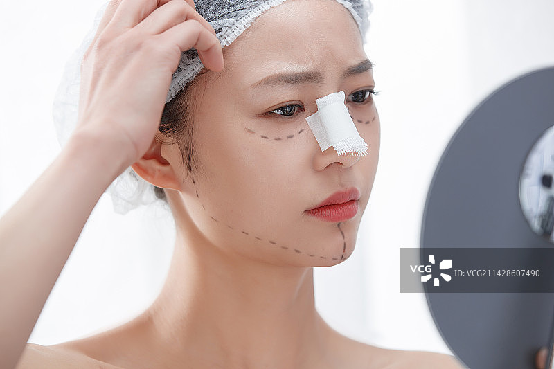 做隆鼻手术的青年女人照镜子图片素材