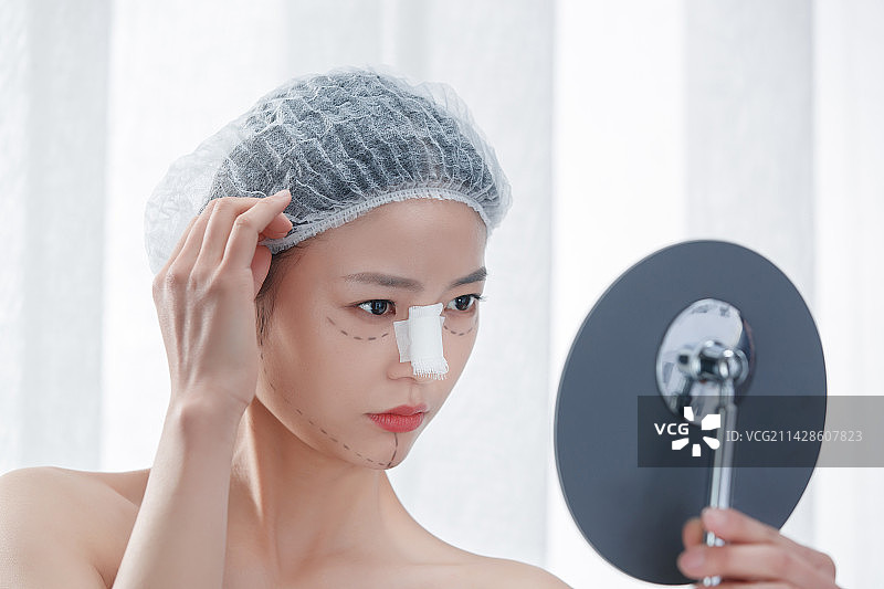 做隆鼻手术的青年女人照镜子图片素材