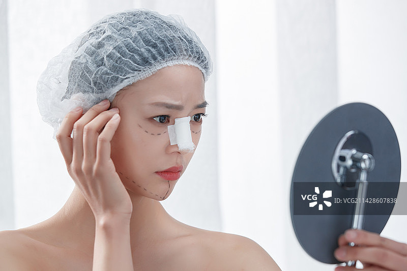 做隆鼻手术的青年女人照镜子图片素材