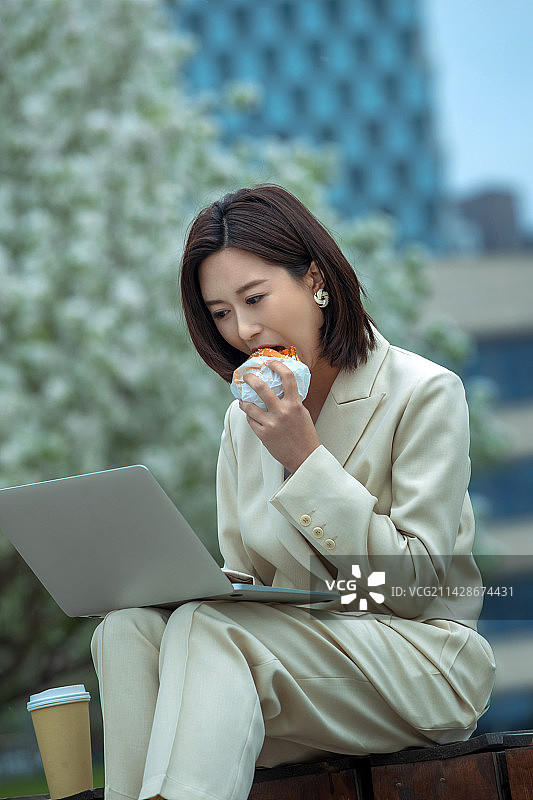 商务女士在户外边吃饭边用电脑图片素材