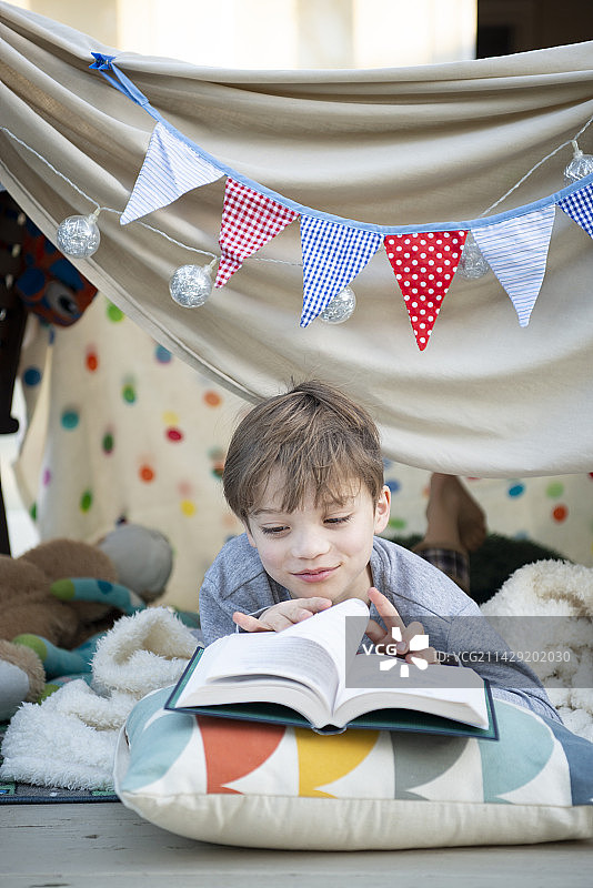 男孩在床单帐篷里看书图片素材