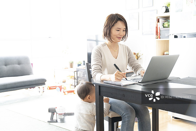 在家用电脑工作的女人和她脚边的婴儿图片素材