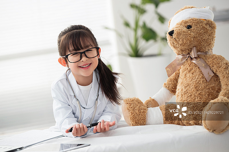 装扮成医生的小女孩给玩具小熊看病图片素材