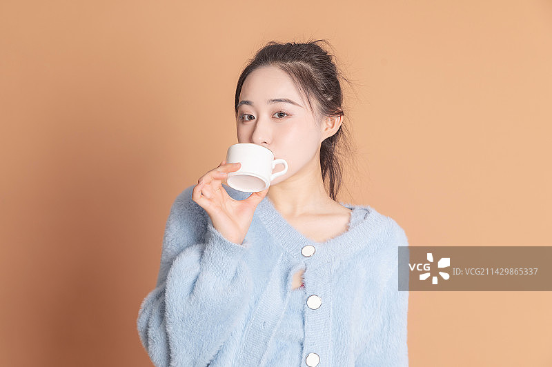 拿着咖啡杯做搞怪表情的时尚女性图片素材