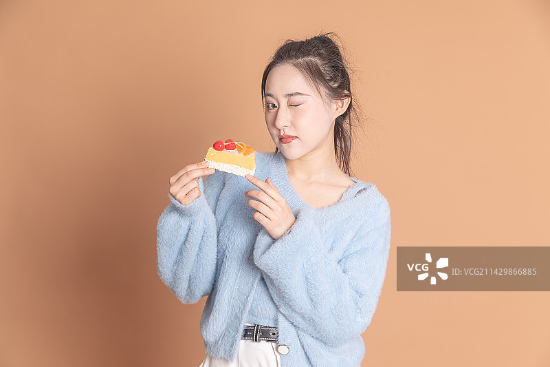 纯色背景前拿着蛋糕甜点的时尚女性图片素材