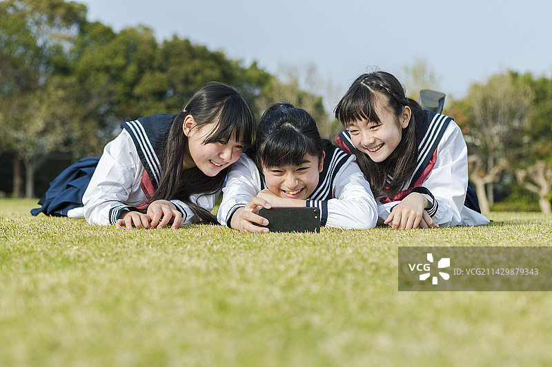 女学生躺在草地上拍照图片素材