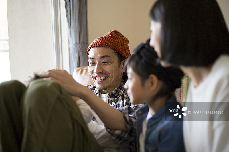 父亲抱着孩子坐在腿上，大女儿和母亲在一旁观看图片素材