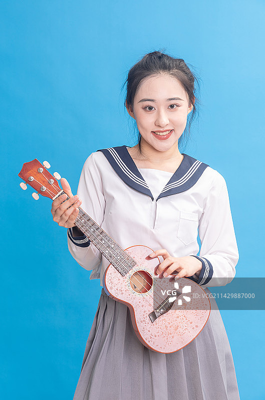 蓝色背景前拿着尤里克克乐器的青年女学生图片素材