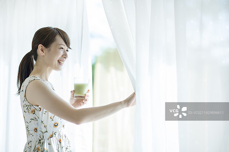 女人拿着冰沙并拉开窗帘图片素材