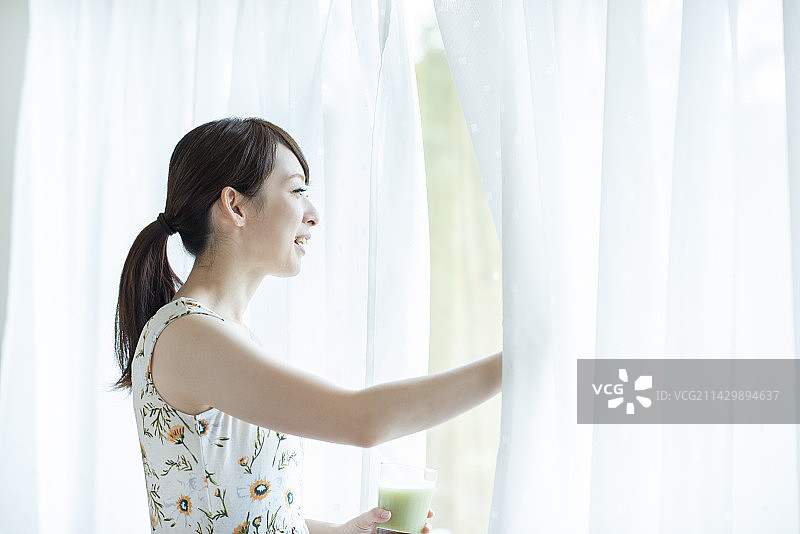 女人拿着冰沙并拉开窗帘图片素材