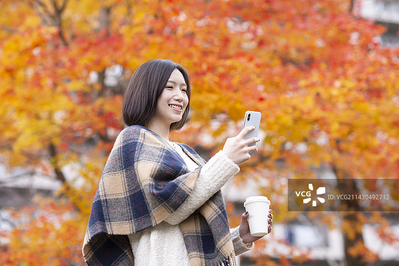 女人在秋叶前操作智能手机图片素材