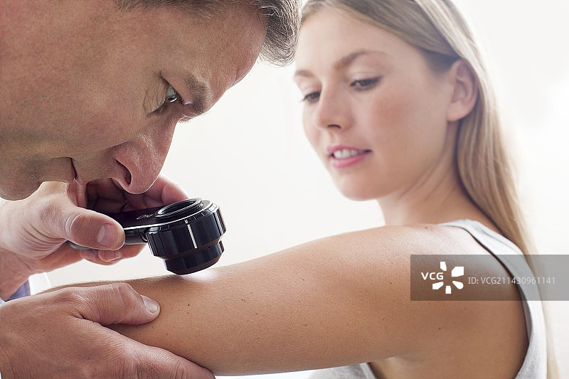 医生检查年轻女子手臂上的痣图片素材