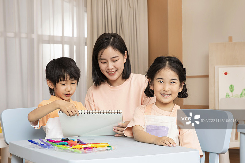 老师坐在桌子旁教教男孩女孩画画图片素材