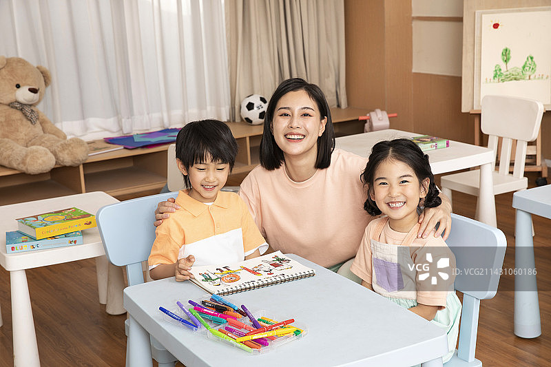 老师坐在桌子旁教教男孩女孩画画图片素材