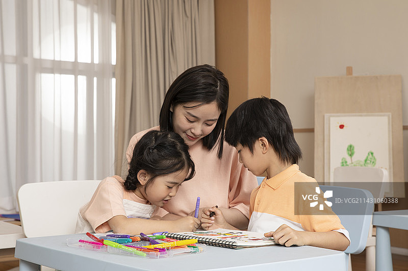 老师坐在桌子旁教教男孩女孩画画图片素材