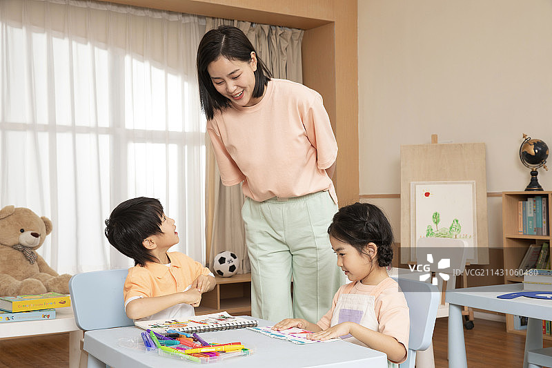 老师坐在桌子旁教教男孩女孩画画图片素材