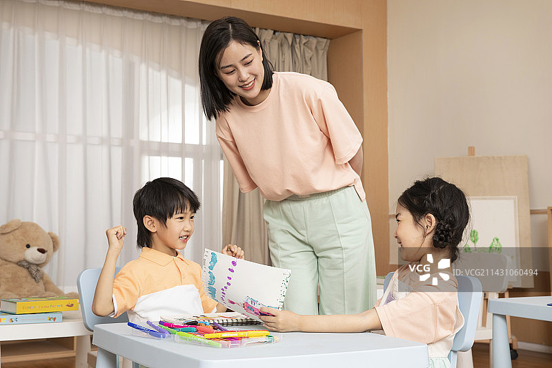 老师坐在桌子旁教教男孩女孩画画图片素材
