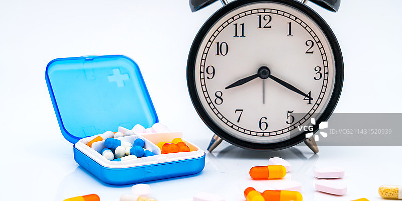 白色背景下的药盒、药片、胶囊和闹钟——按时吃药概念图片素材