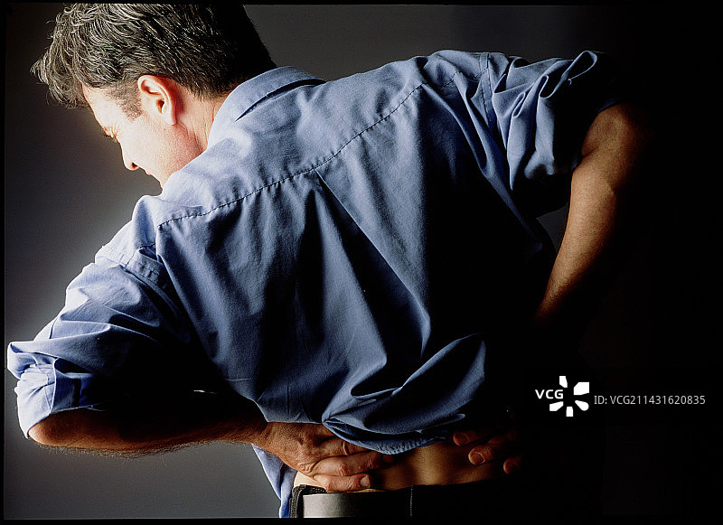 男子因背痛难忍而扶住背部图片素材