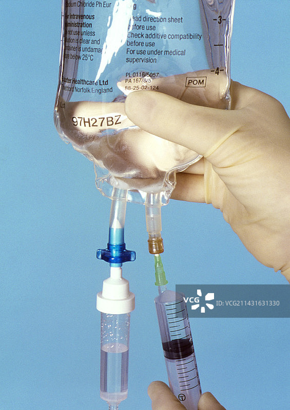 戴手套的手将药物注入静脉滴注袋中图片素材