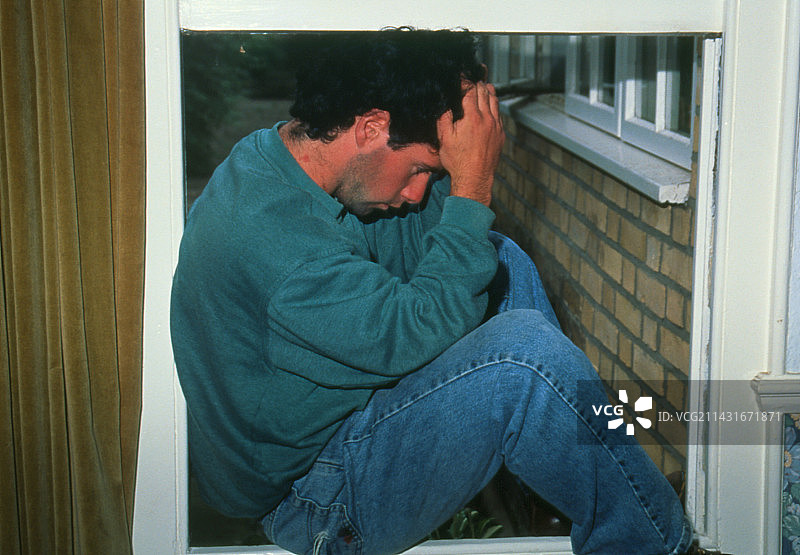 沮丧的年轻男子沮丧地坐在窗边图片素材