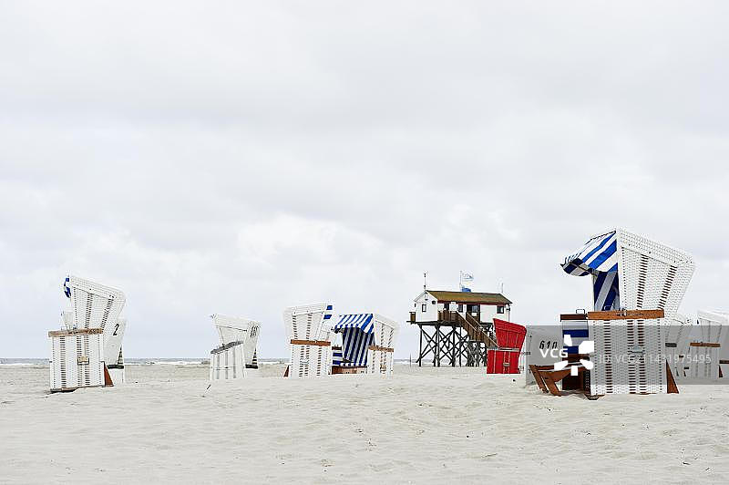 圣彼得-奥尔丁海滩上的带顶棚的柳条沙滩椅，位于高跷房屋前，德国石勒苏益格-荷尔斯泰因图片素材