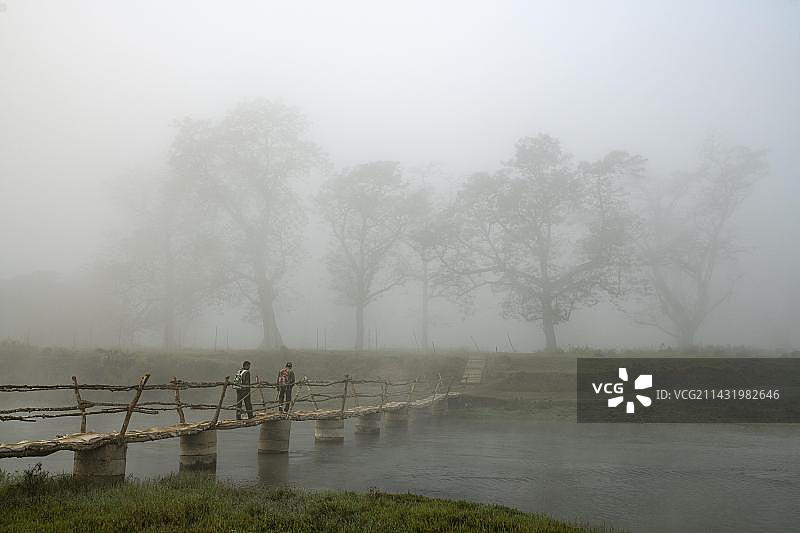 两个男人在尼泊尔奇特旺国家公园拉普蒂河上的桥上晨雾中行走图片素材