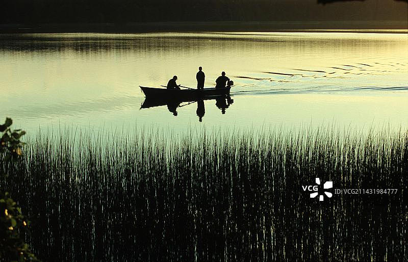 黄昏时分，在波兰马祖里亚莫克雷湖上的一艘船上的垂钓者图片素材