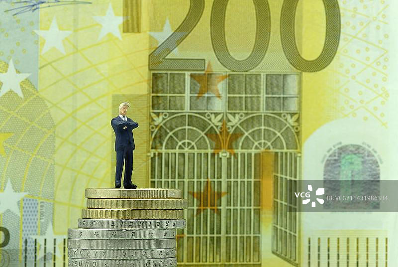 站在硬币堆上，手持200欧元钞票的满意商人图片素材