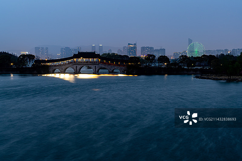 江苏无锡长广溪湿地公园石塘桥廊桥夜景慢门镜头照片背景映衬中的无锡城市建筑景观图片素材