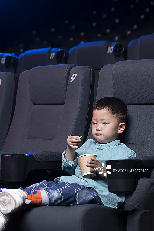 可爱的男孩在电影院看电影 拿着爆米花桶图片素材