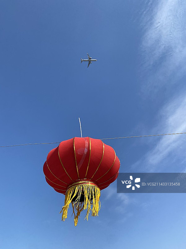 站在红灯笼下抬头看到飞机飞过，蓝天下形成了一副美好的画面图片素材