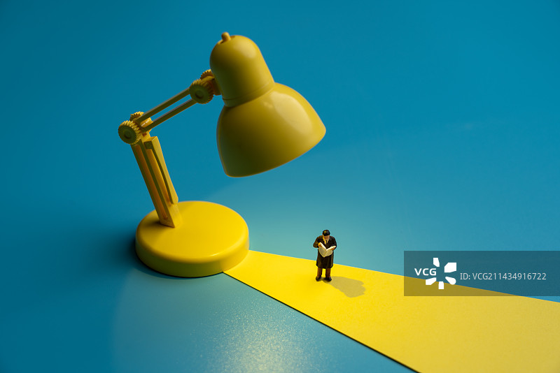 蓝色背景中站在黄色台灯下看书看报的男士微缩创意图片素材