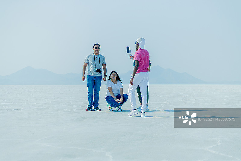 年轻的朋友们在白色沙滩上用自拍杆合影，背景是晴朗的天空，博纳维尔盐滩，犹他州，美国图片素材