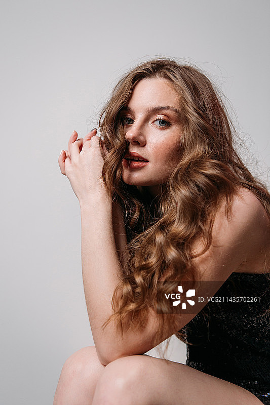 身穿黑色亮面连衣裙的女孩坐在白色背景前，俄罗斯图片素材