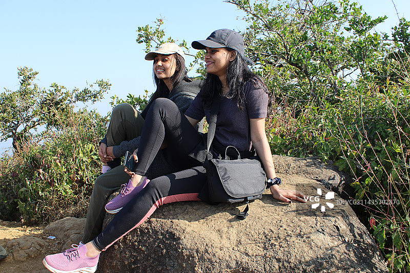 微笑的朋友们坐在岩石上，背景是晴朗的天空图片素材