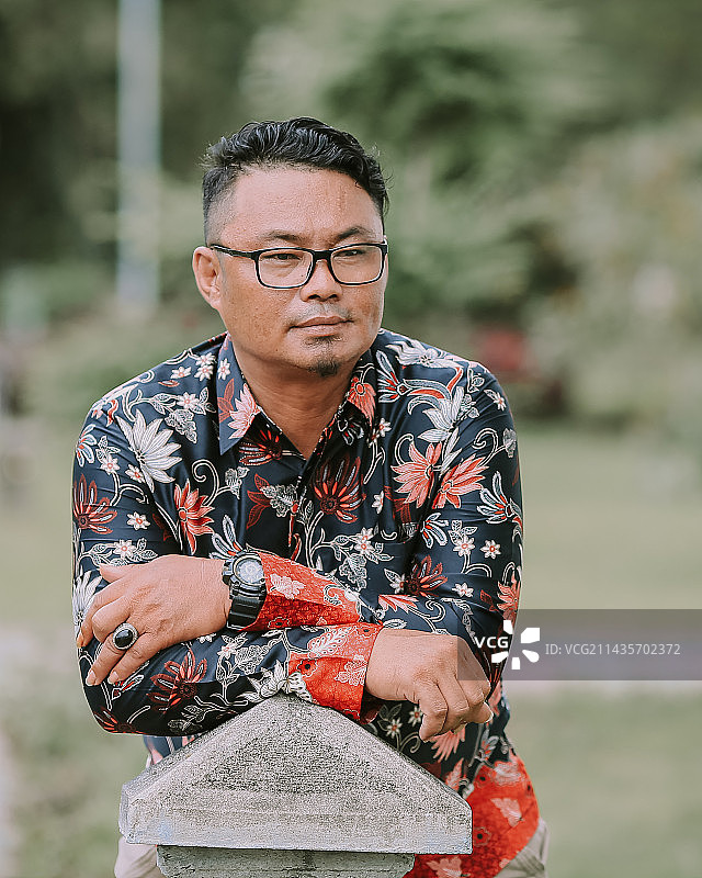 戴眼镜的亚洲男人在户外石头柱子上休息图片素材