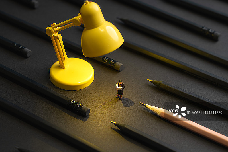 黑色铅笔周围黄色台灯下站着看报的人微缩创意图片素材