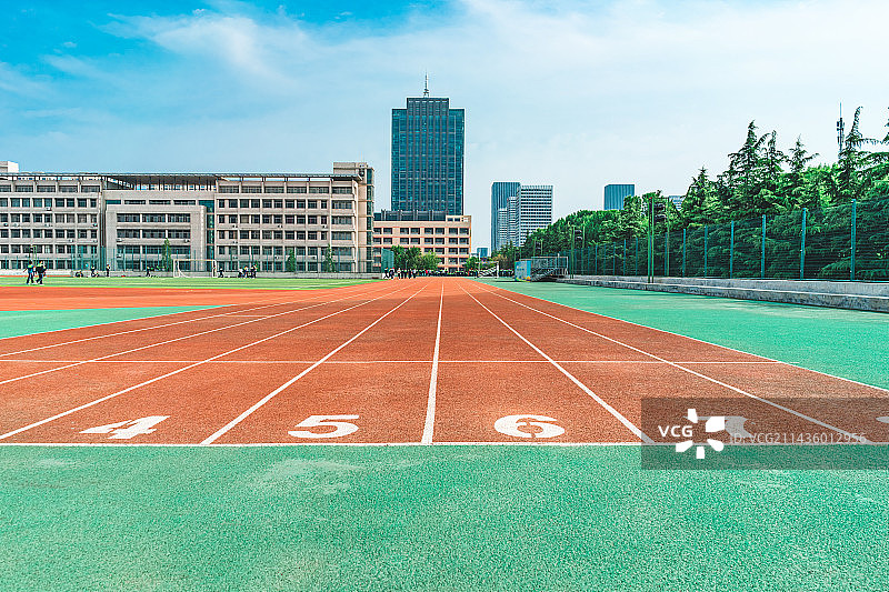 中国学校操场拍摄主题，红色塑胶跑道，绿色的操场，远处的高楼大厦，户外白昼无人图像摄影图片素材