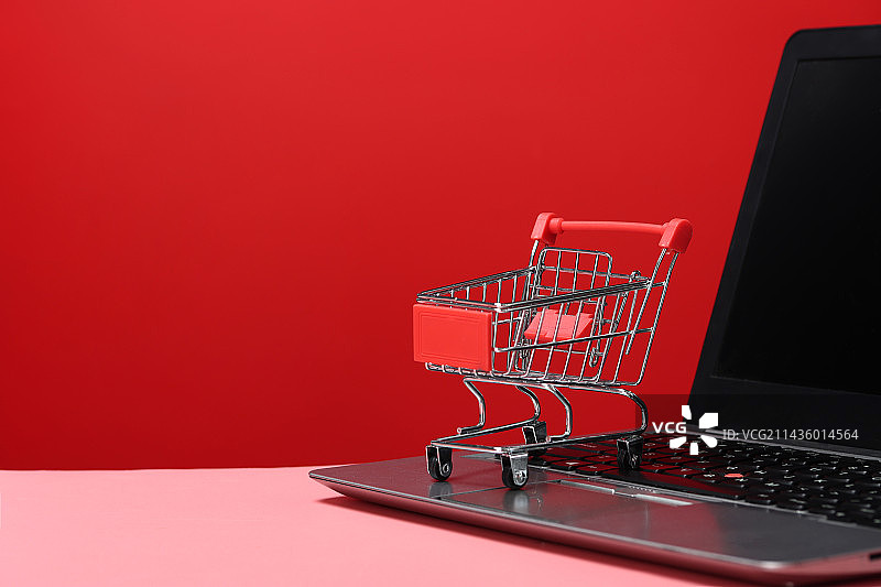 红色背景下的购物车和笔记本电脑特写镜头图片素材