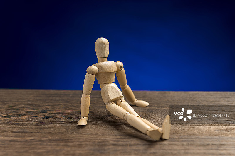 做出各种姿势的木人偶摆放在木桌面上蓝色背景图片素材