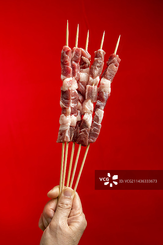 女性手拿鲜羊肉串特写红色背景图片素材