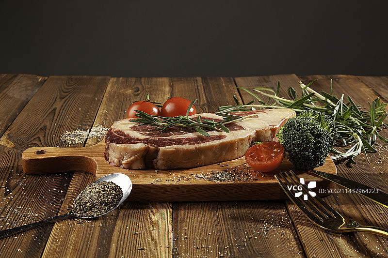 木桌子上的牛眼肉，小番茄，迷迭香，刀叉，西兰花图片素材